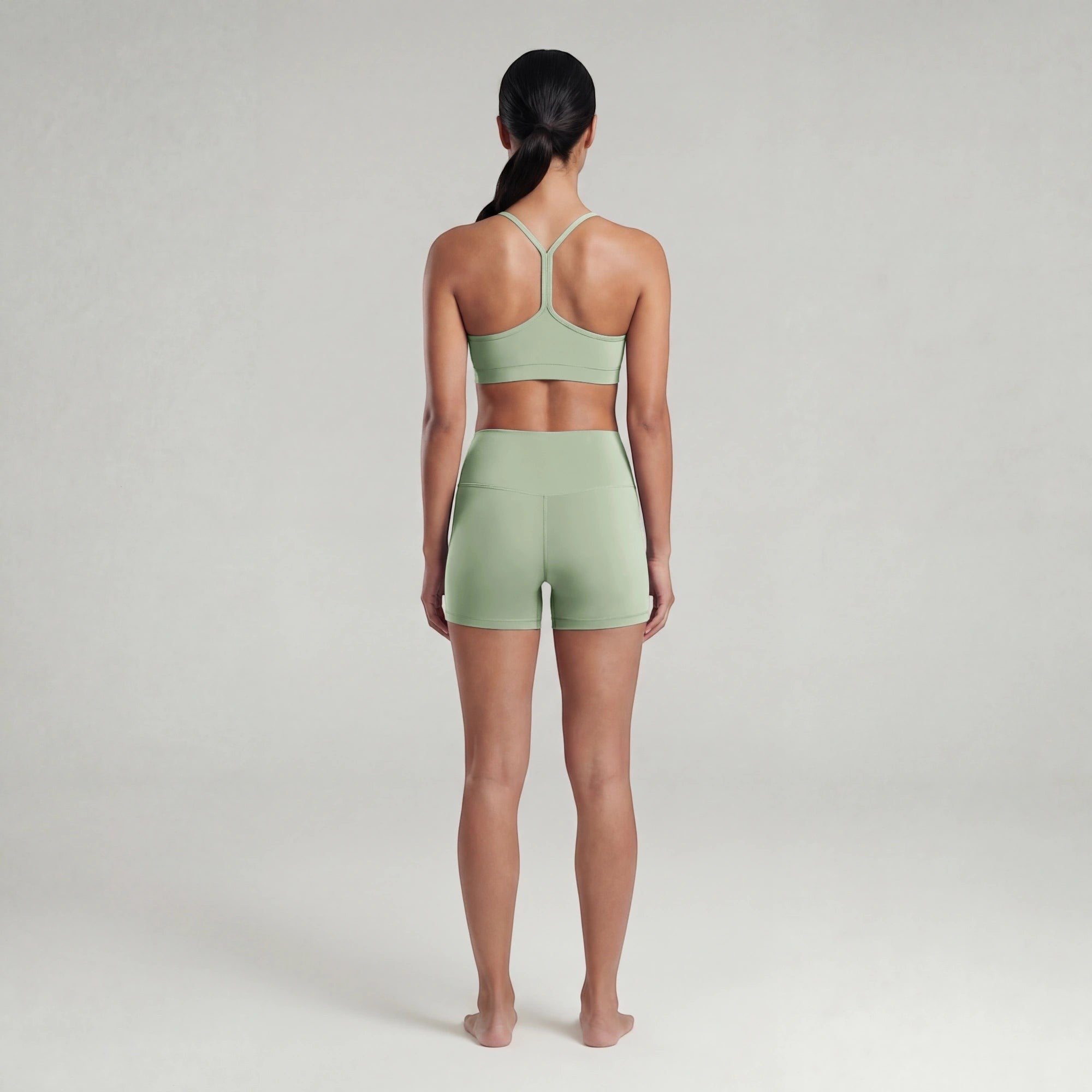 Woman wearing a green sports bra and shorts set on a plain background