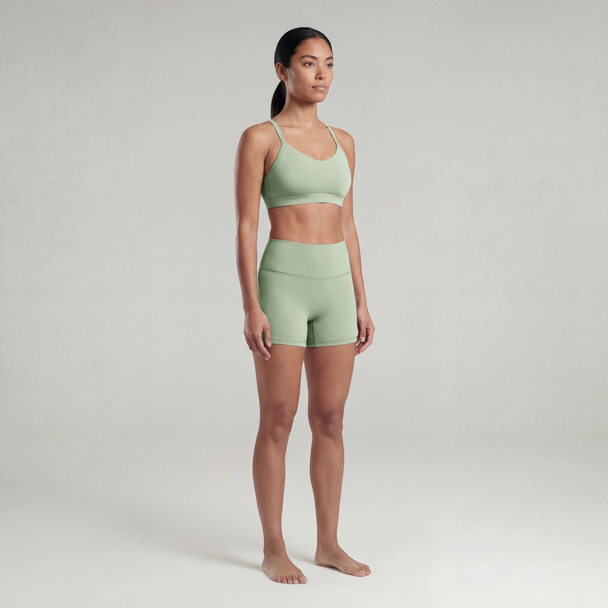 Woman wearing a green sports bra and shorts set on a plain background