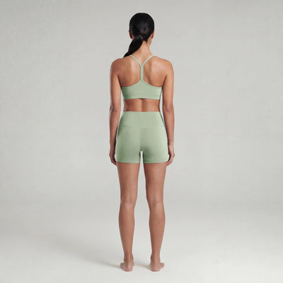 Woman wearing a green sports bra and shorts set on a plain background