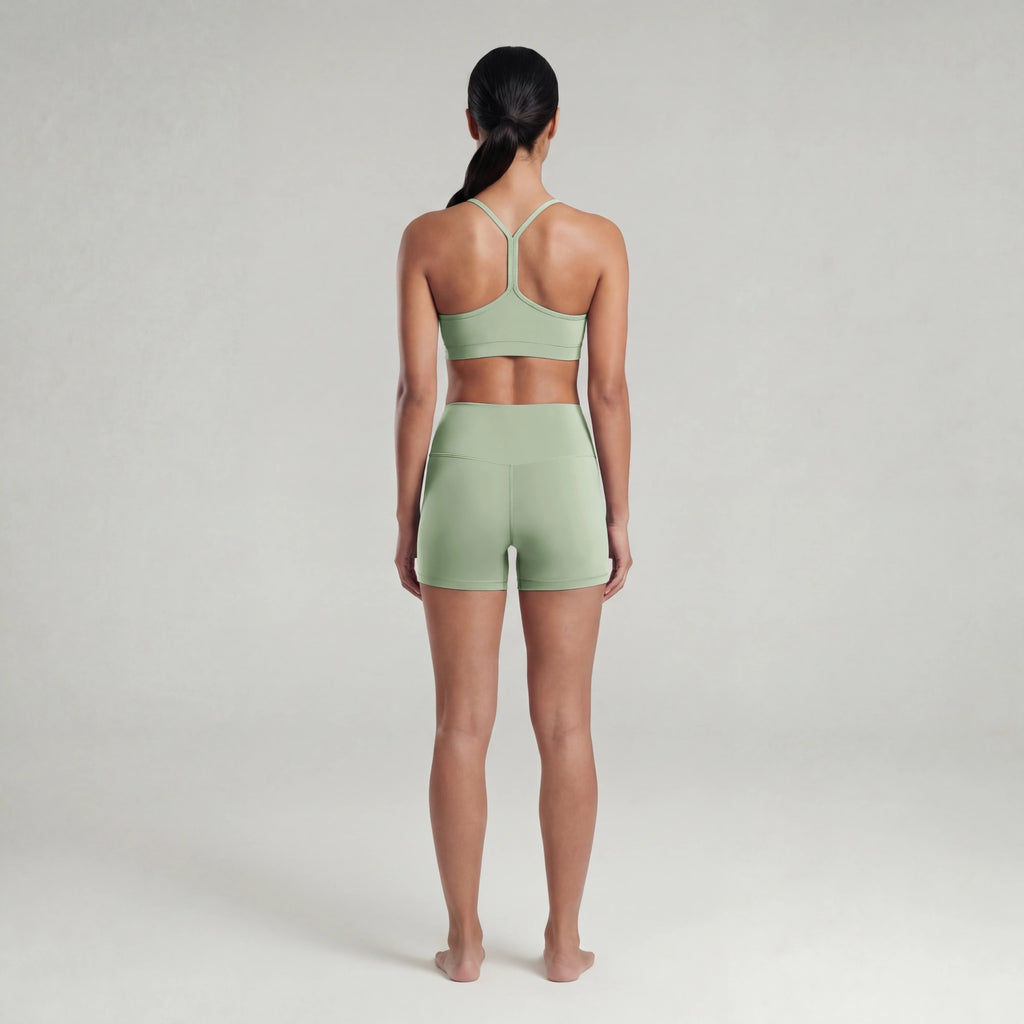 Woman wearing a green sports bra and shorts set on a plain background