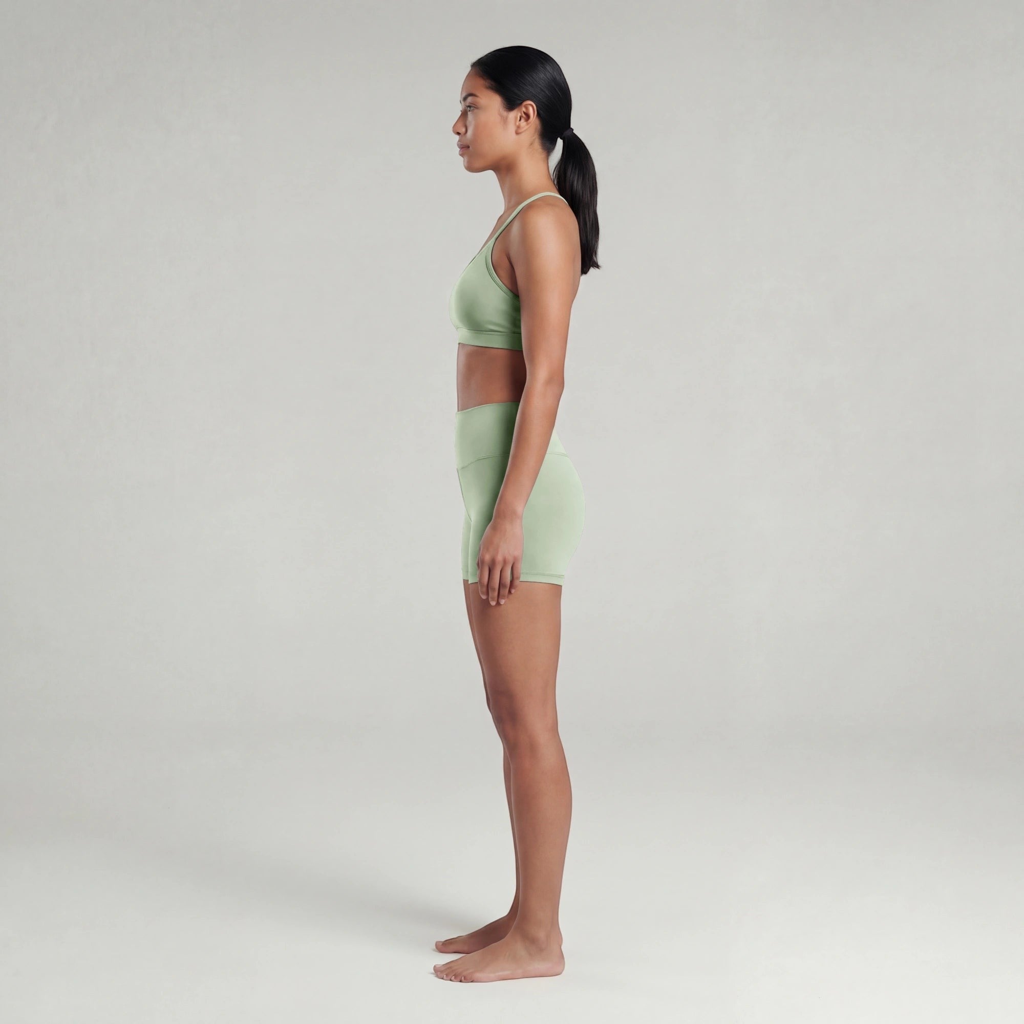 Woman wearing a light green sports bra and shorts on a plain background