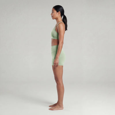 Woman wearing a light green sports bra and shorts on a plain background