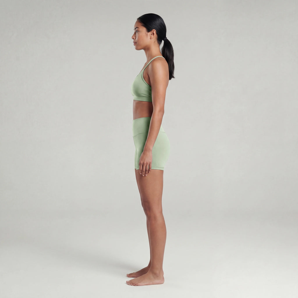 Woman wearing a light green sports bra and shorts on a plain background