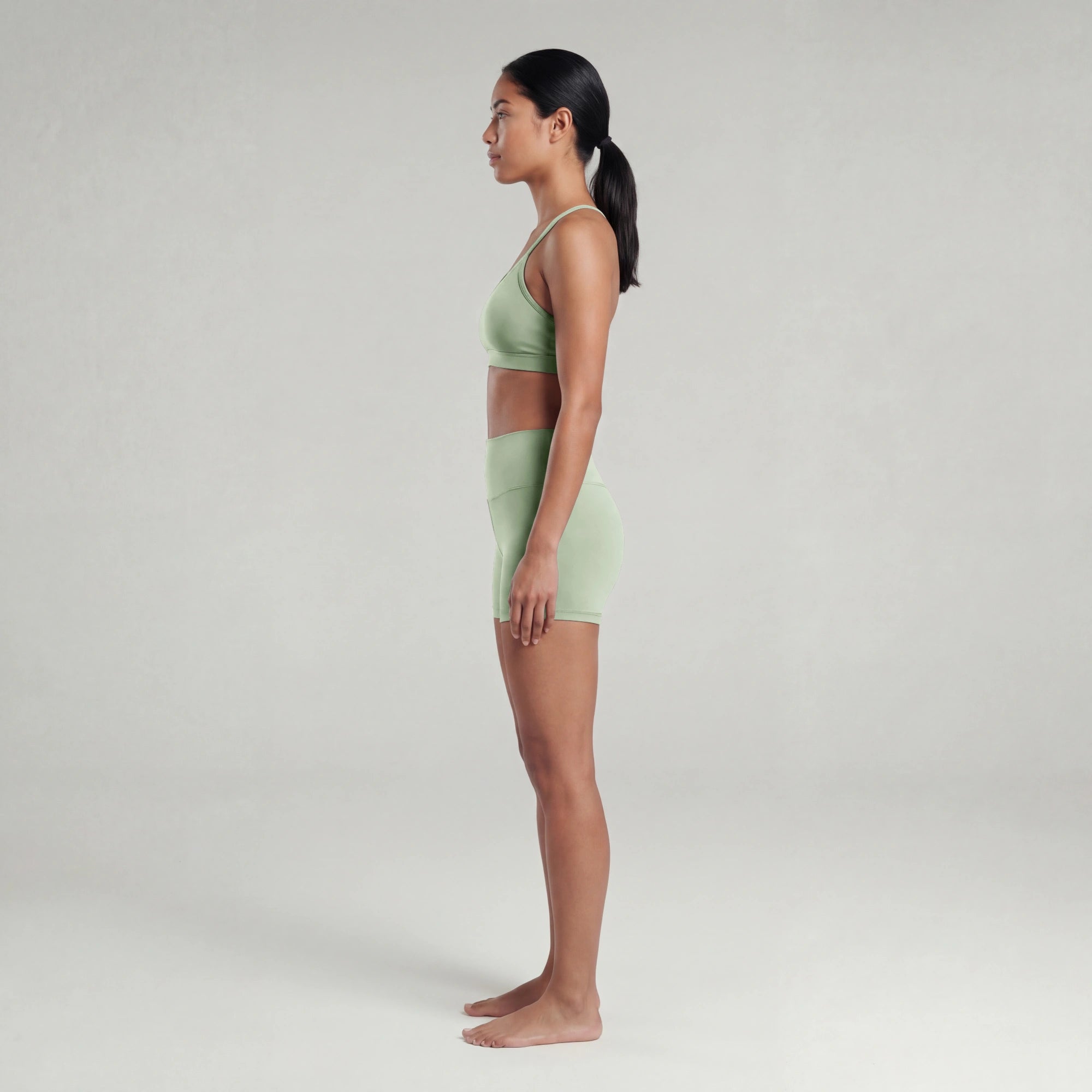 Woman wearing a light green sports bra and shorts on a plain background