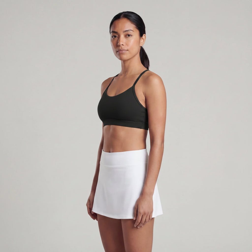 Woman wearing a navy sports bra and white skirt on a plain background
