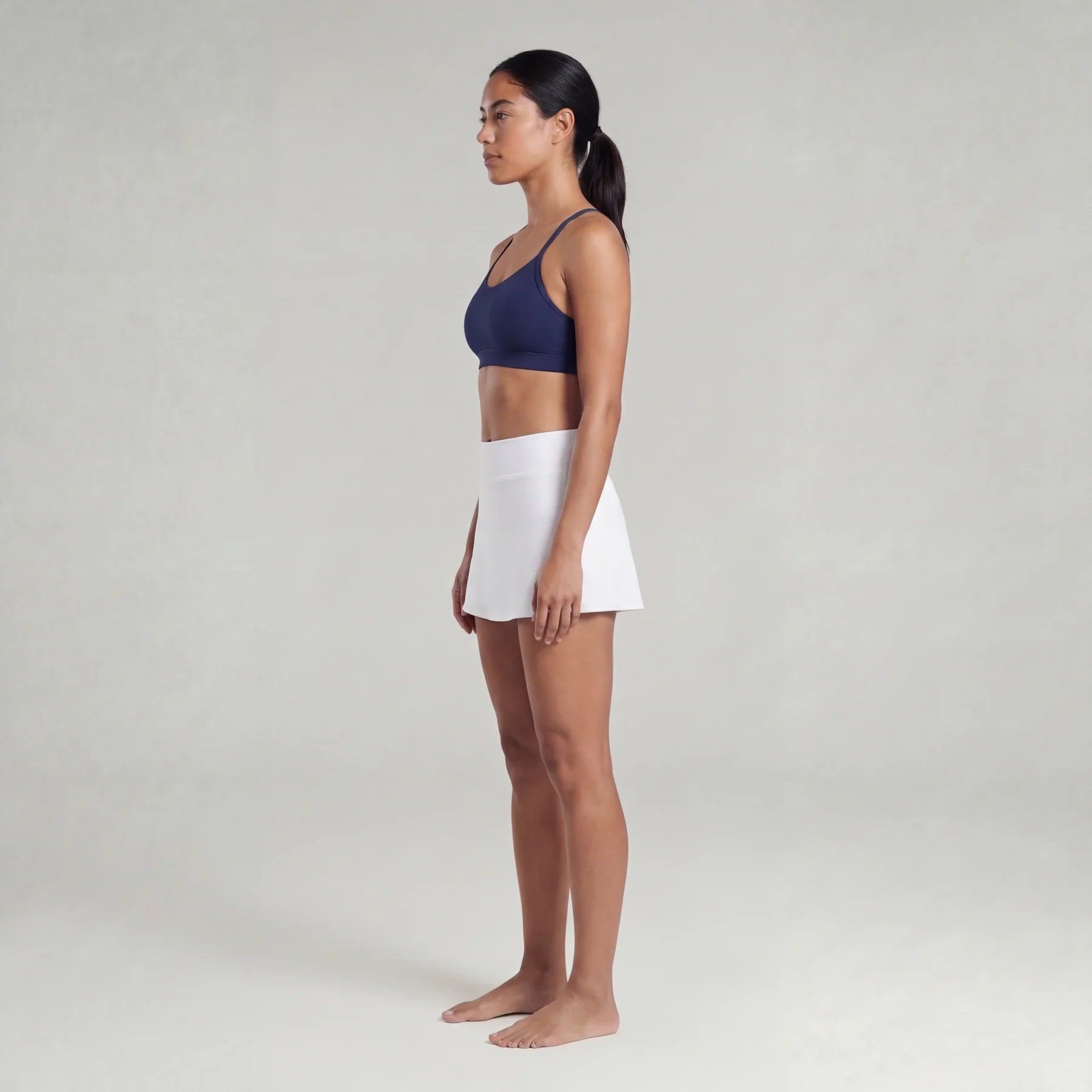 A woman wearing a sports bra and a white skirt on a plain background